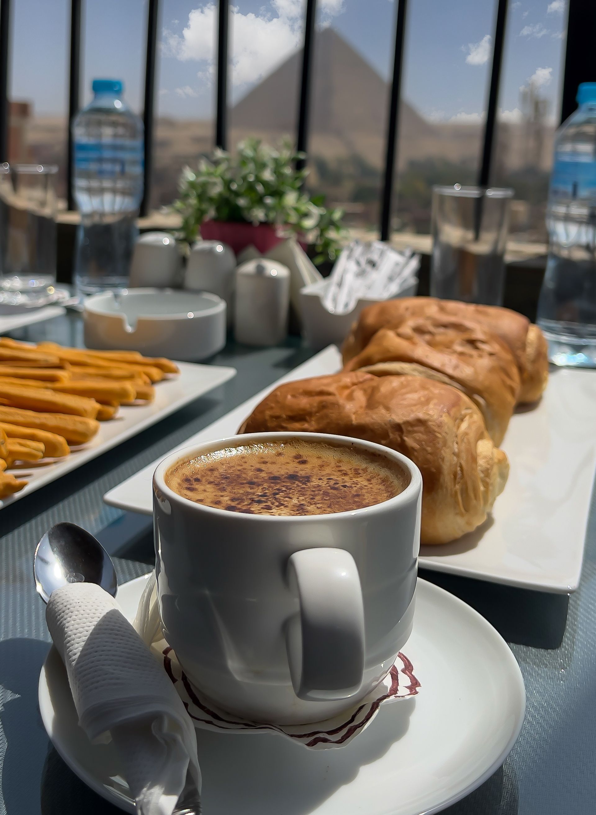 Coffee cup with pastries and churros on a table, pyramids visible in the background.