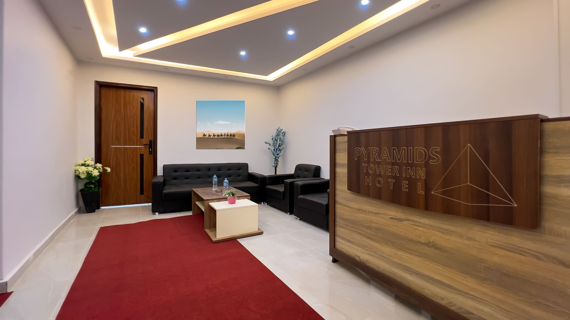 Reception area with red rug, black furniture, and wooden reception desk. Painting of a desert landscape hangs on the wall.