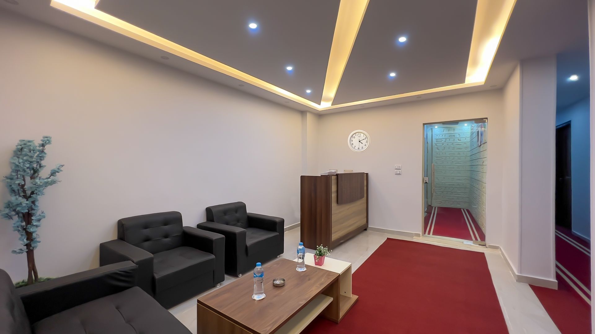 Reception area with black seating, wooden reception desk, and red carpet.