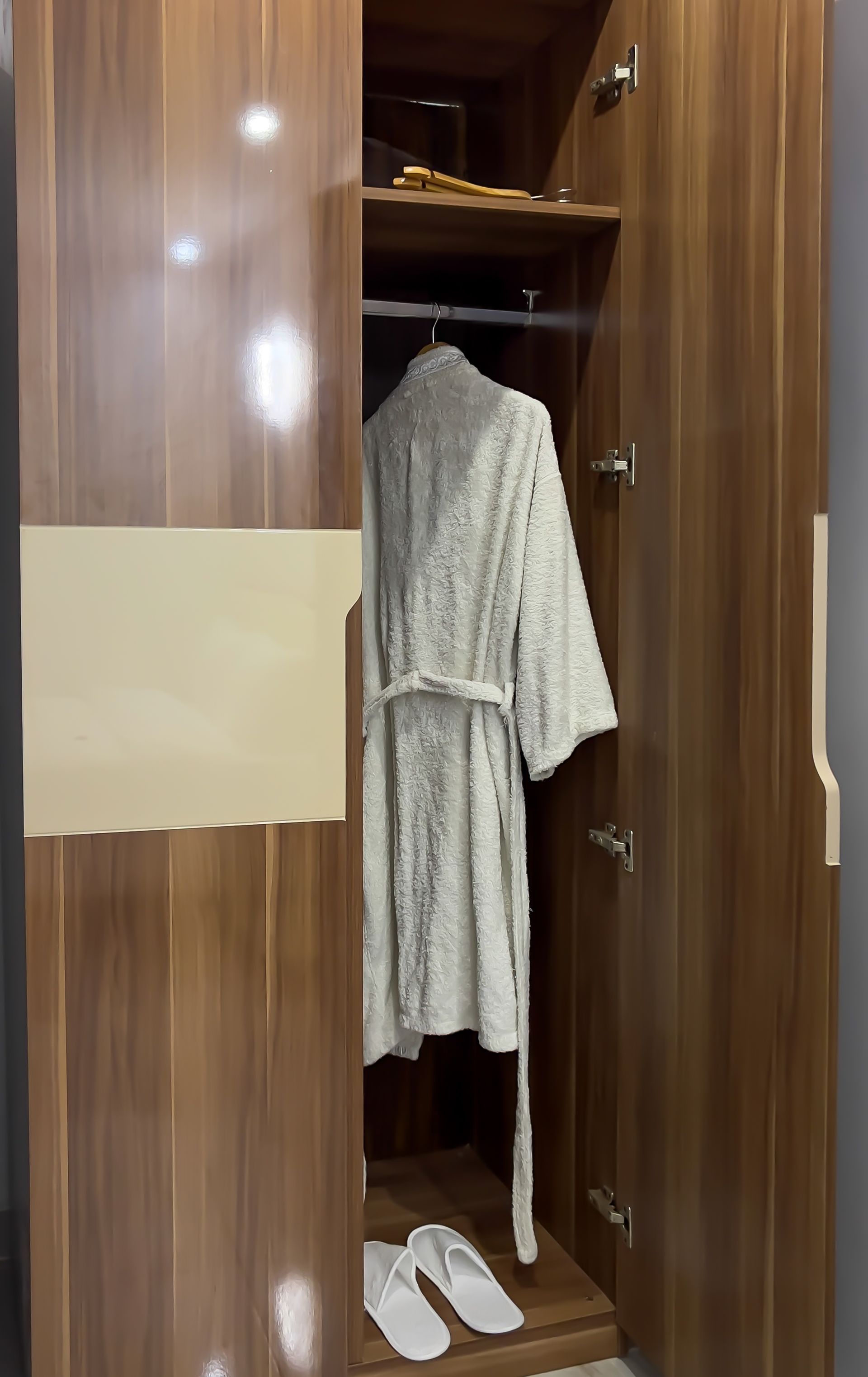 Wooden wardrobe with beige accent, open to reveal a robe and slippers.