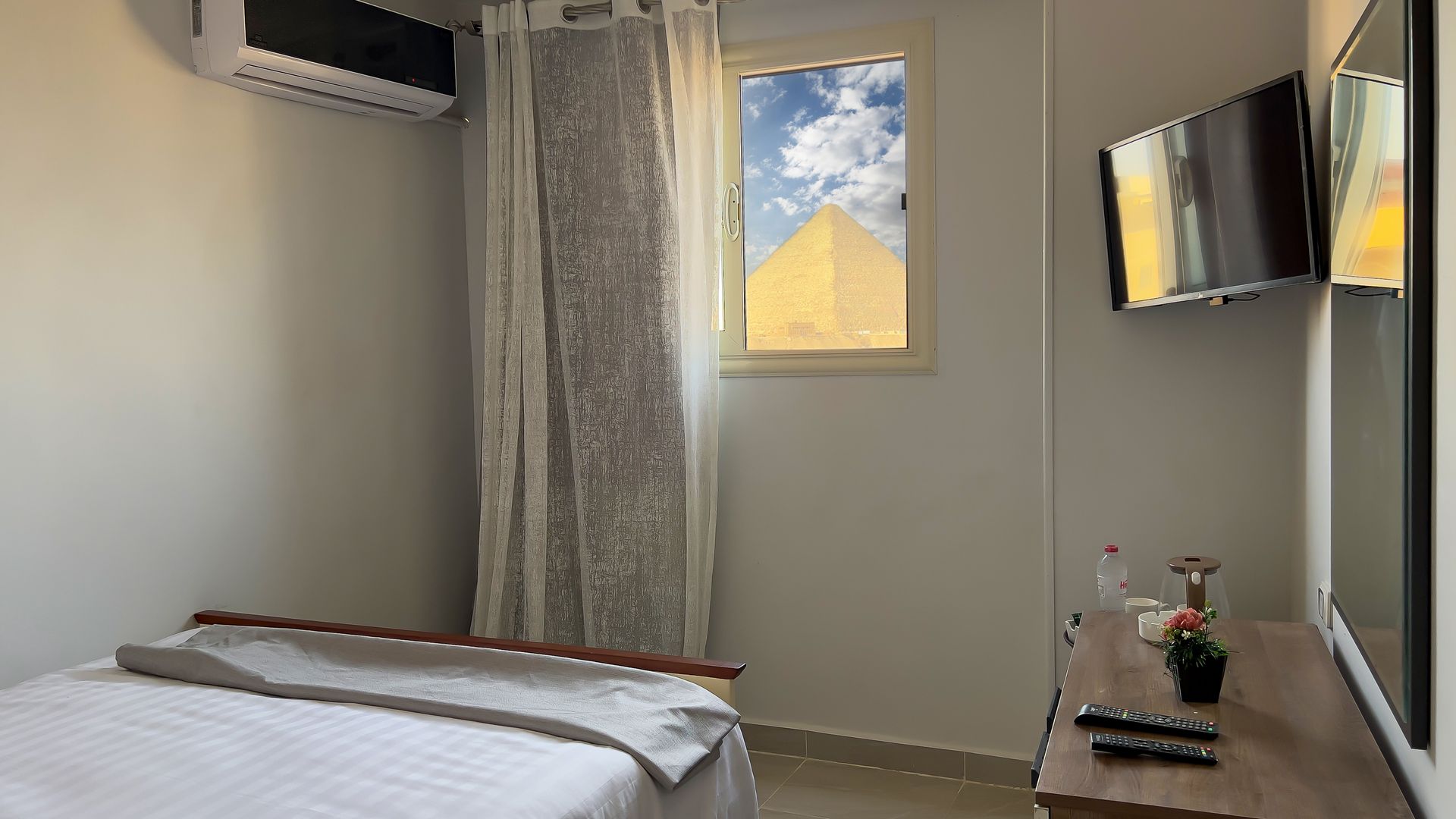 Small hotel room with bed, window with a pyramid view, and wall-mounted TV.