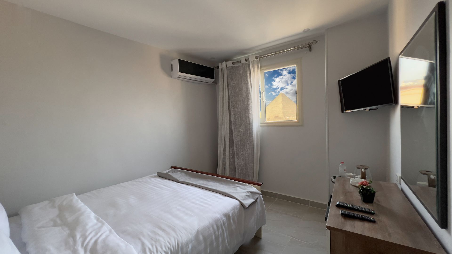 Small hotel room with a single bed, TV, and window with a view of a pyramid.