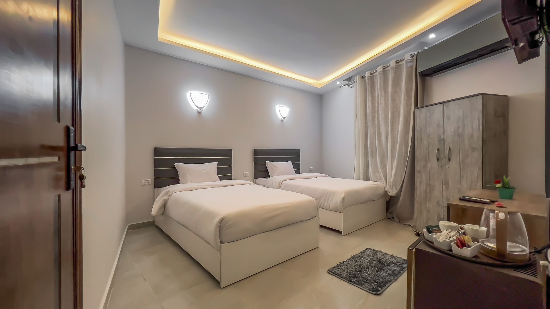 A hotel room with two twin beds, a wardrobe, and a small table with tea.