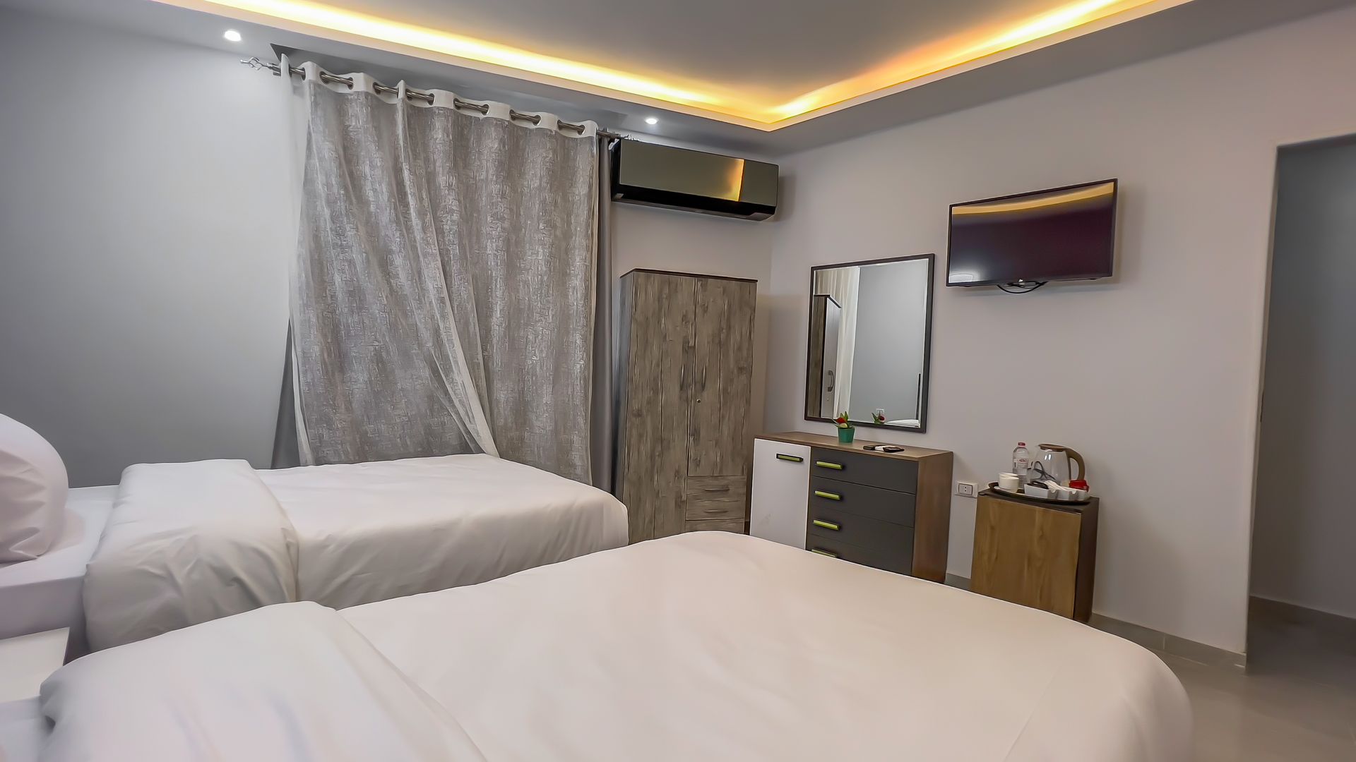 Hotel room with two beds, TV, mirror, and a small refrigerator.