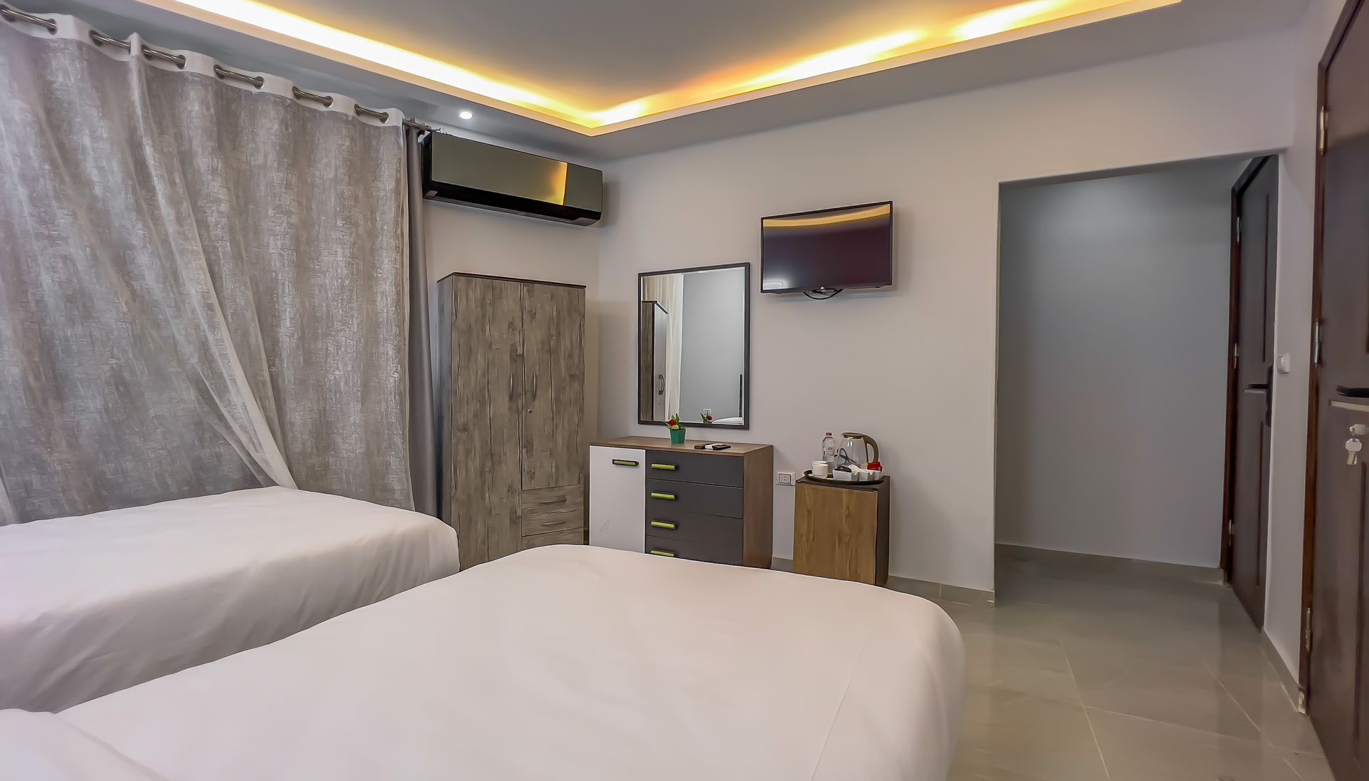Bedroom with two beds, a cabinet, mirror, TV, and open doorway.