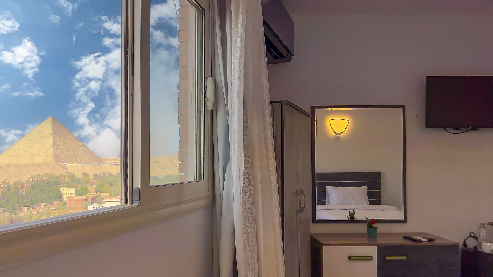Room with window view of Egyptian pyramids. Reflective mirror and TV on wall.