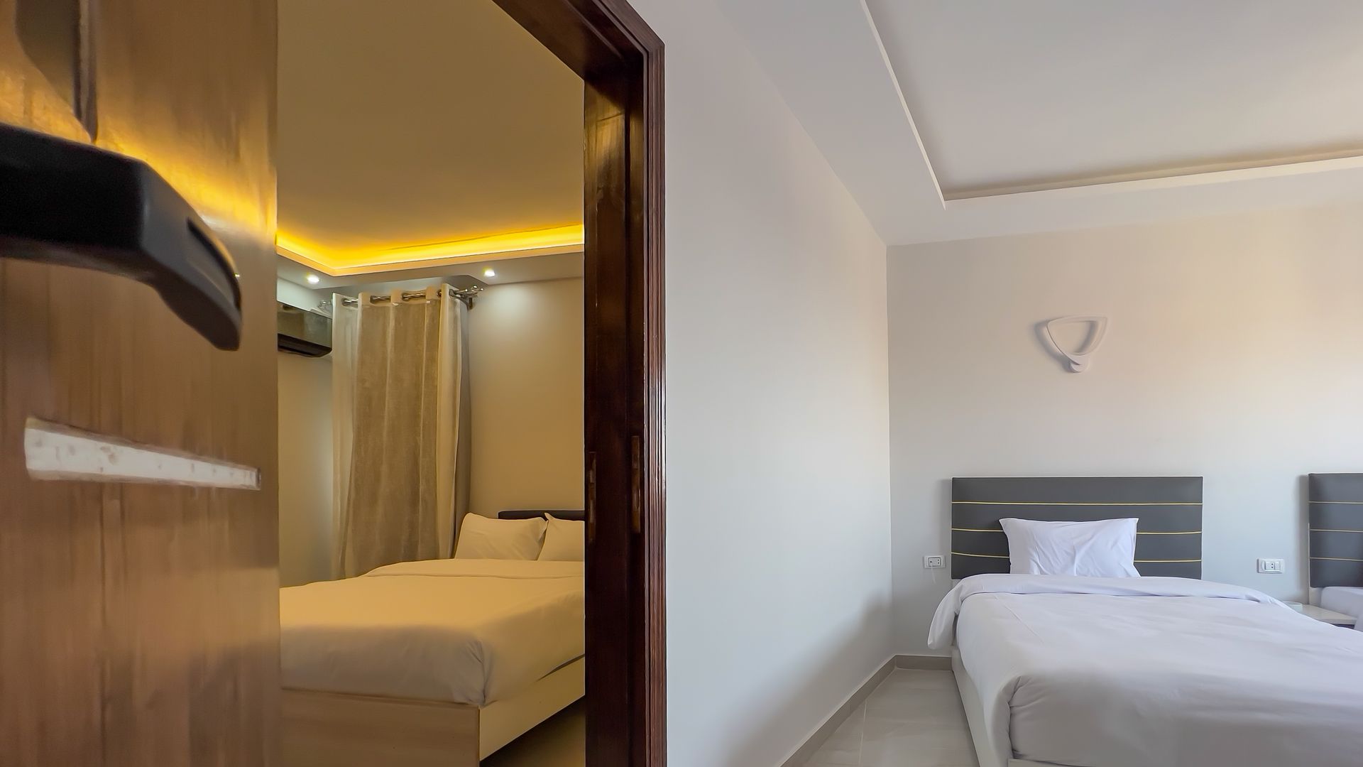Two hotel bedrooms, one visible in reflection. Beds with white linens, neutral walls.