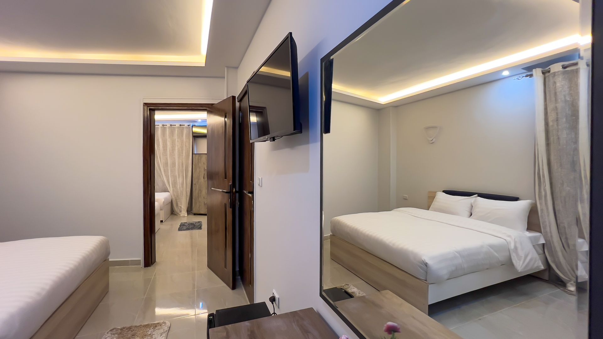 Bedroom interior with a large mirror reflecting a bed, TV, and open doorway to another room.