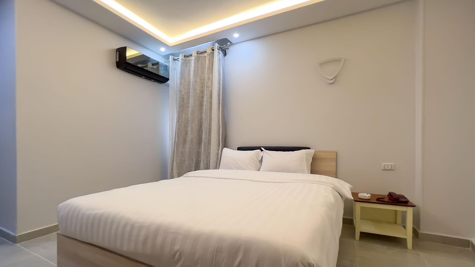 Bedroom with white bedding, curtains, and walls, featuring a bed and small table.