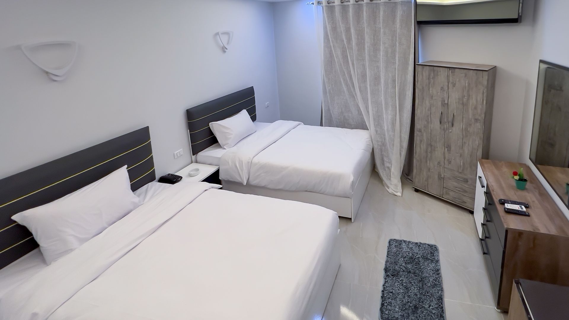 Bedroom with two beds, white bedding, gray headboards, and a wooden wardrobe.