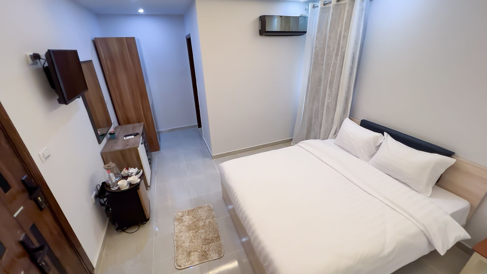Bedroom with a white bed, wooden wardrobe, a TV, and a neutral rug on the floor.