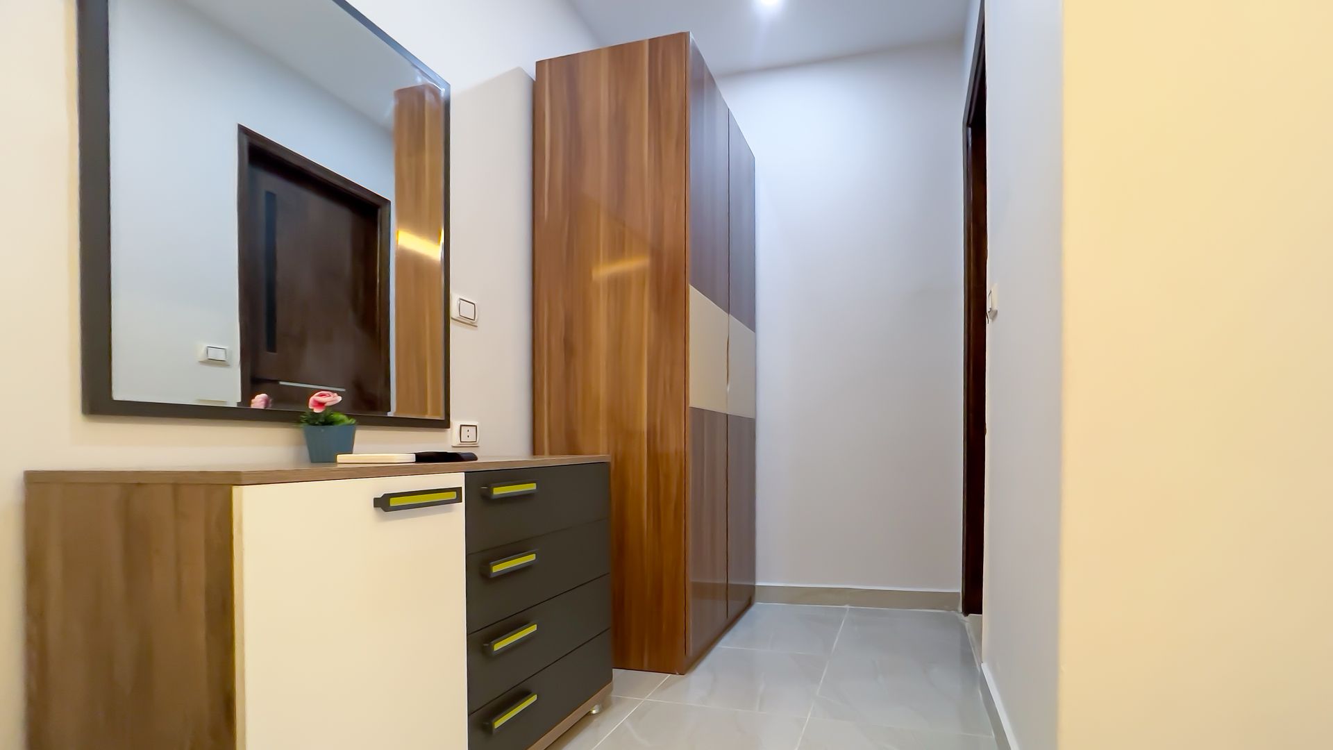 A hallway with a dresser, mirror, and closet with wood and white panels. A dark doorway is visible.