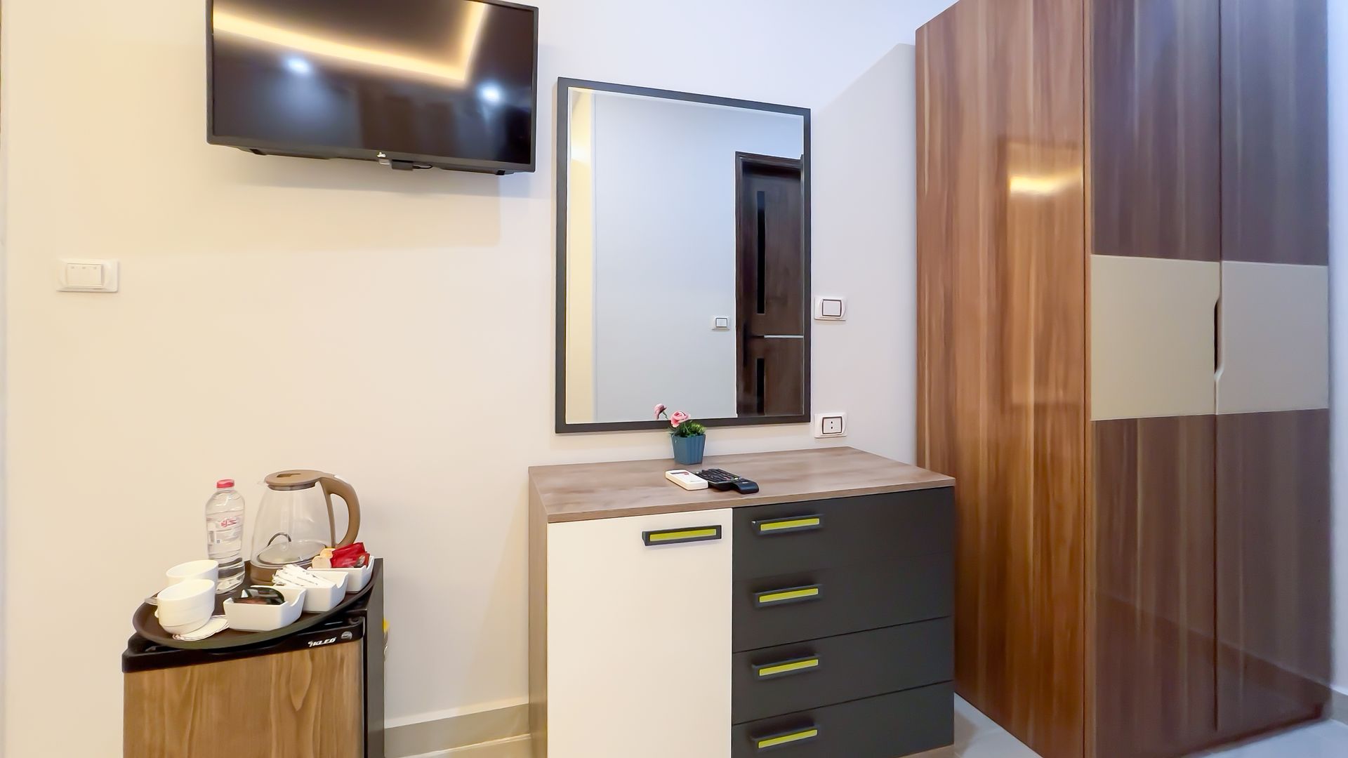 Hotel room interior with TV, mirror, dresser, and wardrobe.