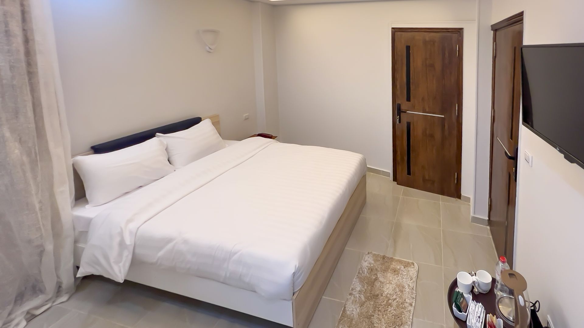 Bedroom with a large bed, door, and a television. Neutral color scheme, clean, well-lit.