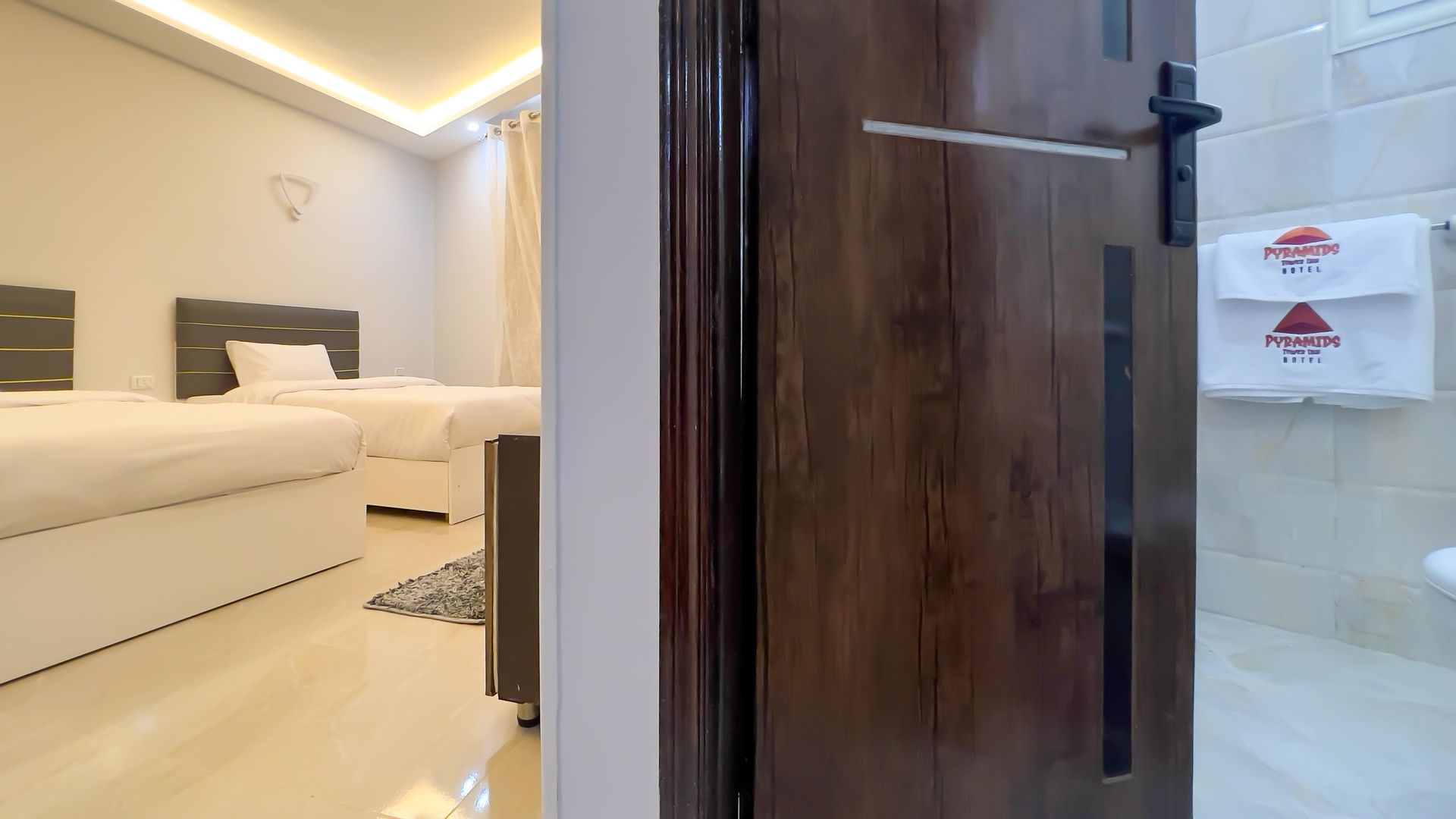 Open wooden door revealing a bedroom with two beds and a glimpse of a bathroom with towels.