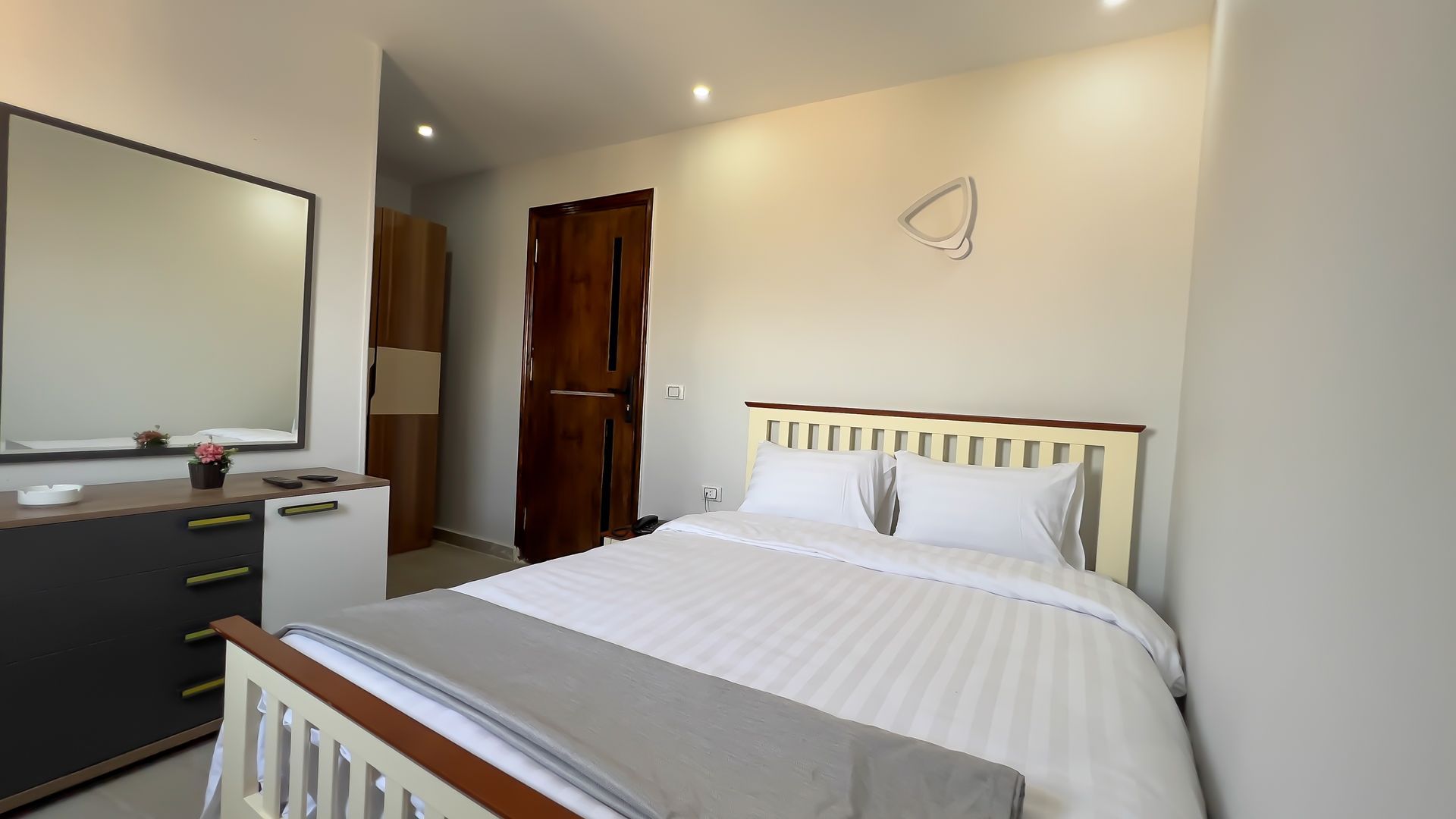 Bedroom with a double bed, dresser, large mirror, and brown wardrobe.