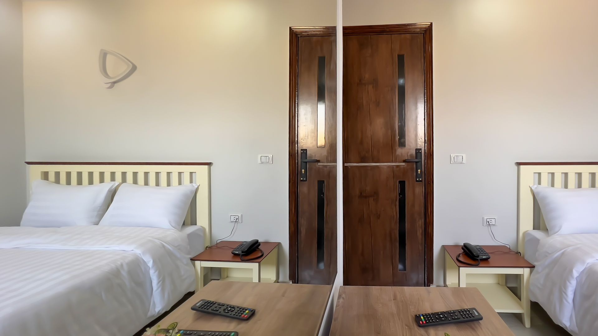 Two beds with white linens, a wooden door, and a mirror in a light-colored room.