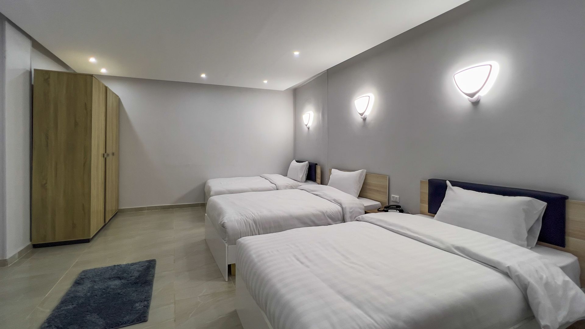 A hotel room with three beds, a wooden closet, and wall-mounted lights.