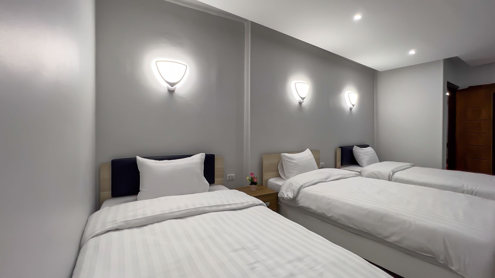 Three single beds in a gray hotel room with wall-mounted lamps.