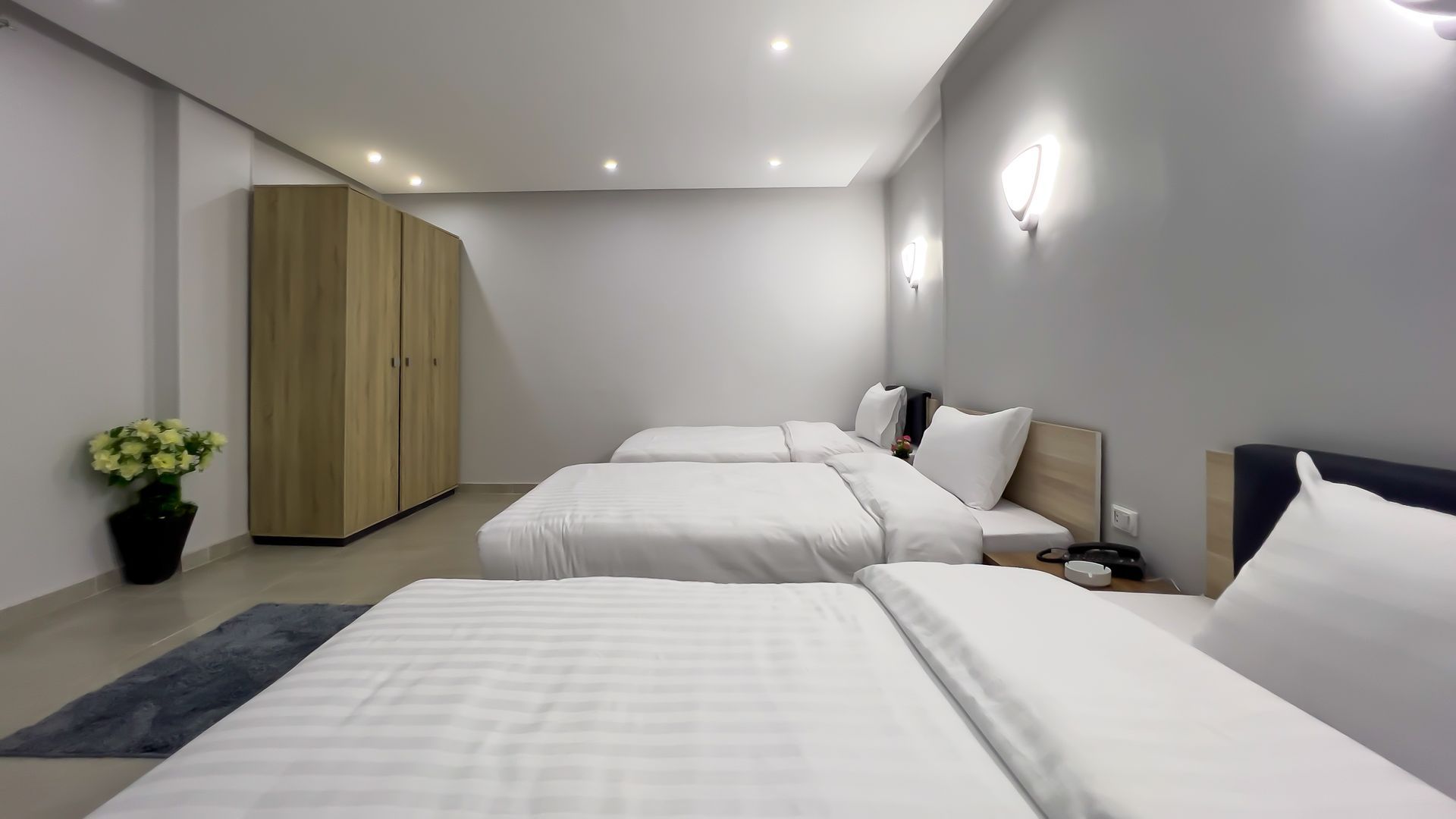 Bedroom with three beds, white bedding, wooden wardrobe, and gray walls.