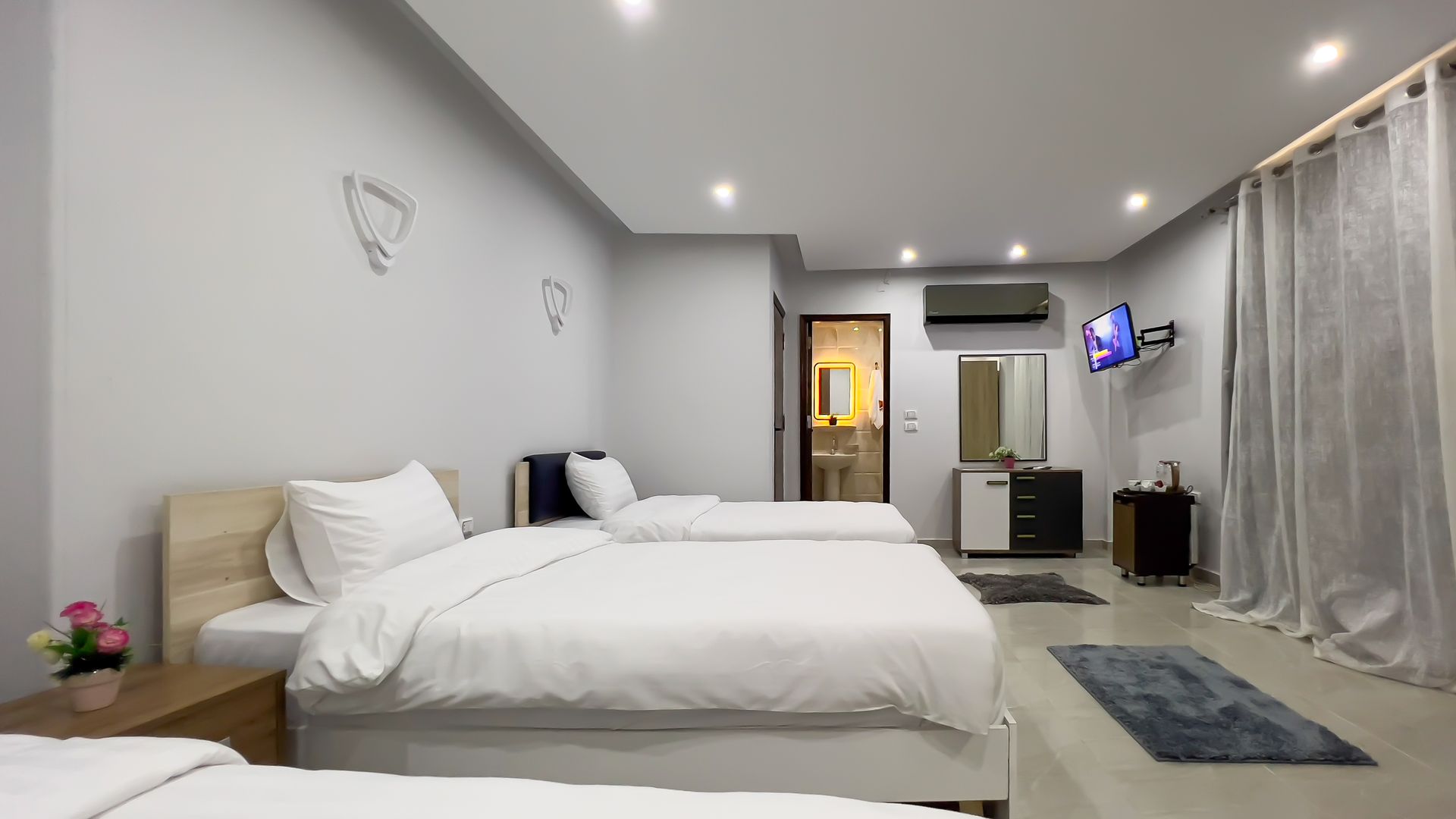 Hotel room with three beds, gray walls, TV, and bathroom door.