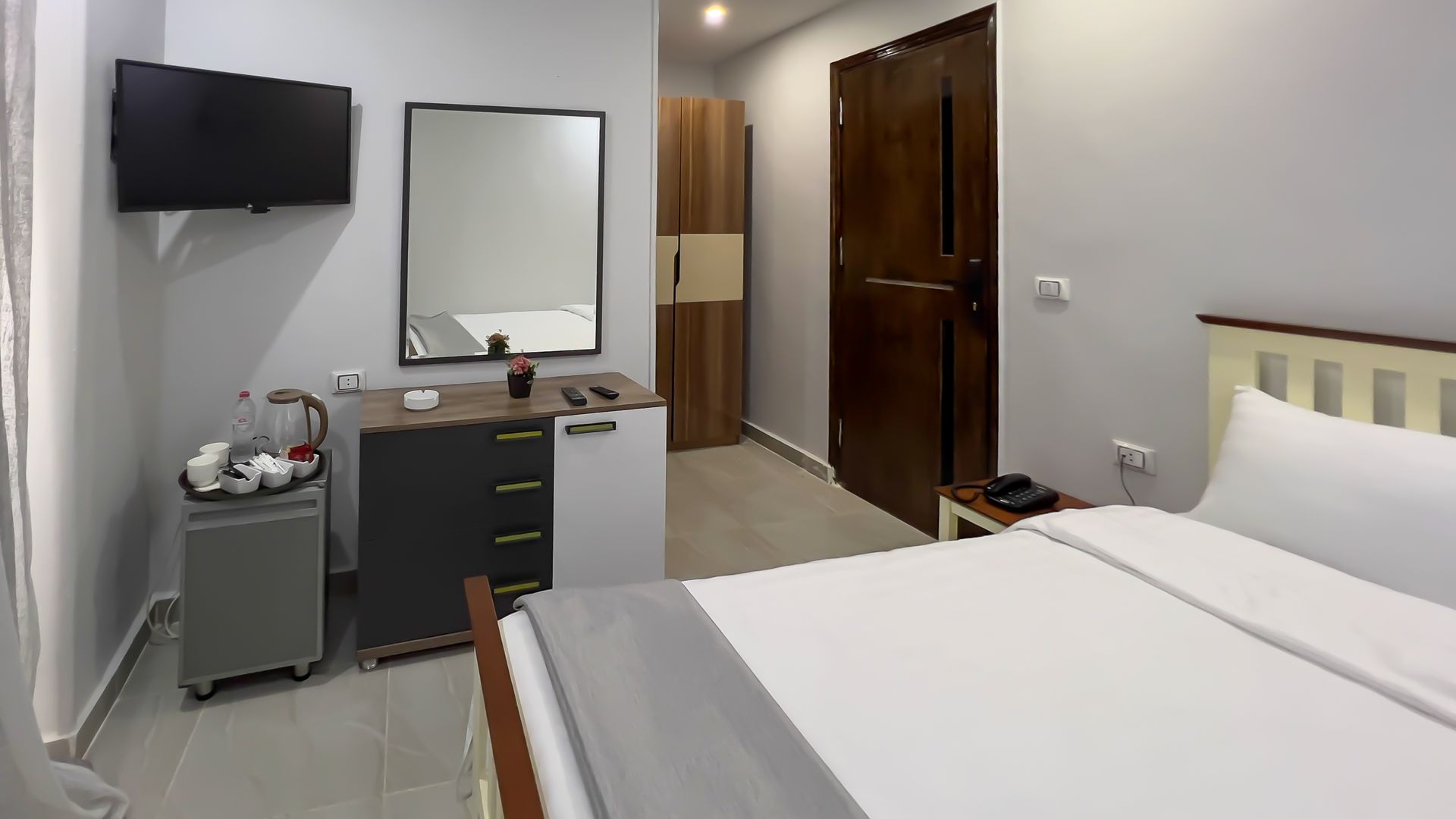 Hotel room interior with a bed, TV, mirror, and small refrigerator.