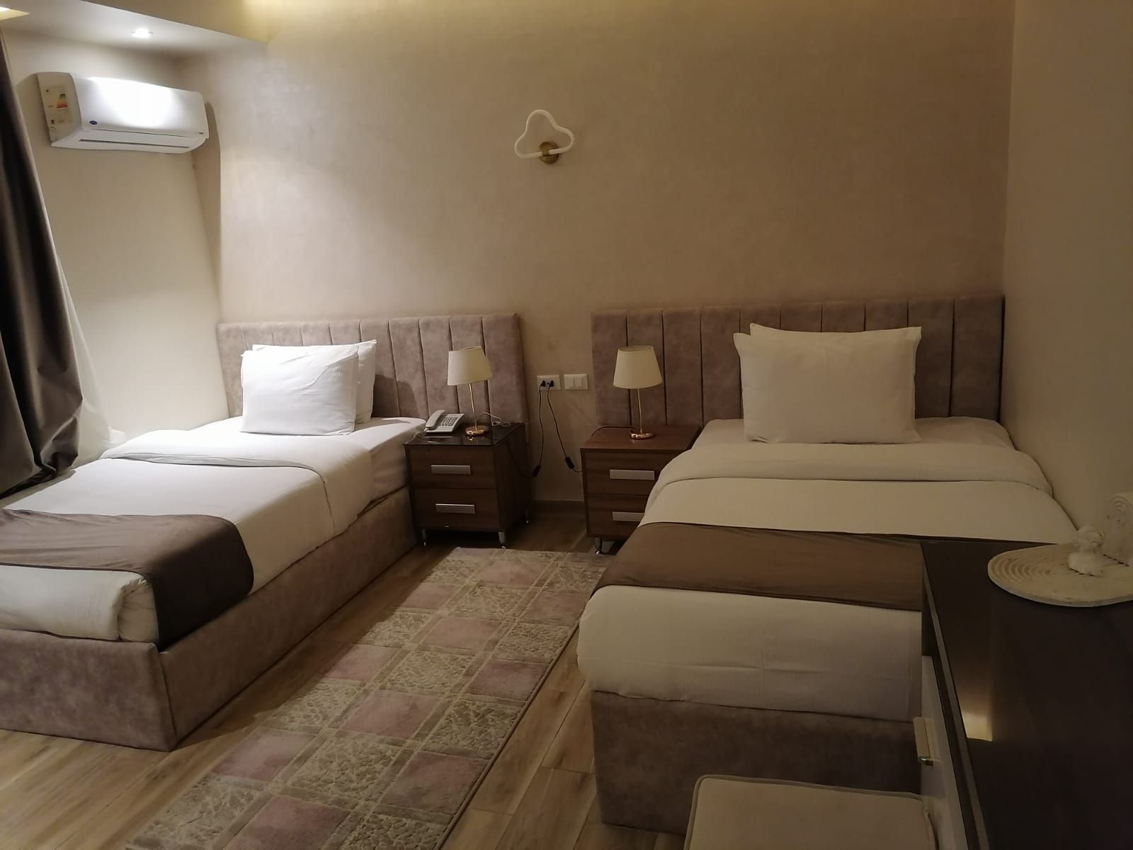 A hotel room with two twin beds, a wooden closet, curtains, and a small table.