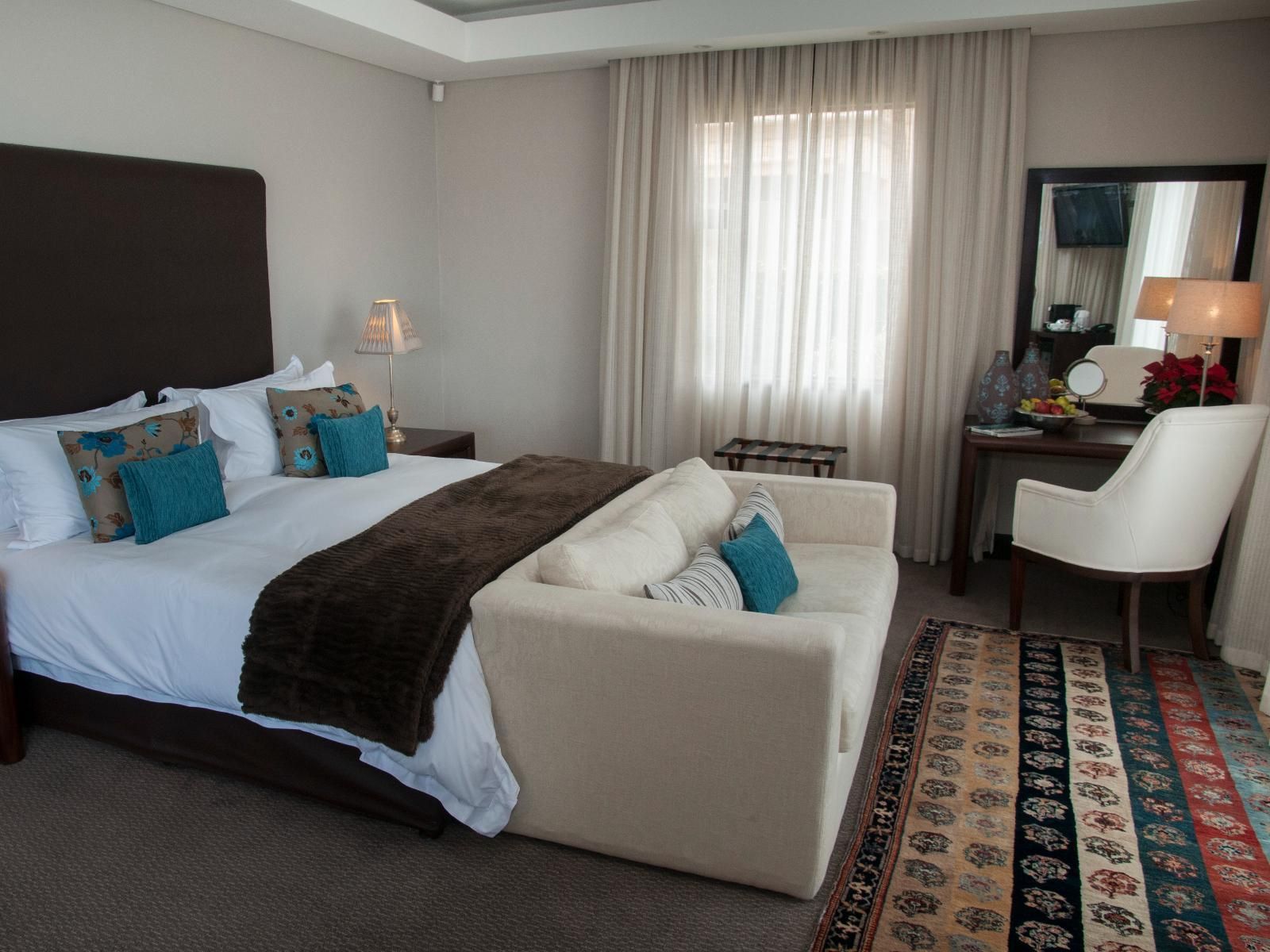 Bedroom with king-size bed, white sofa, vanity, window with sheer curtains, and patterned rug.