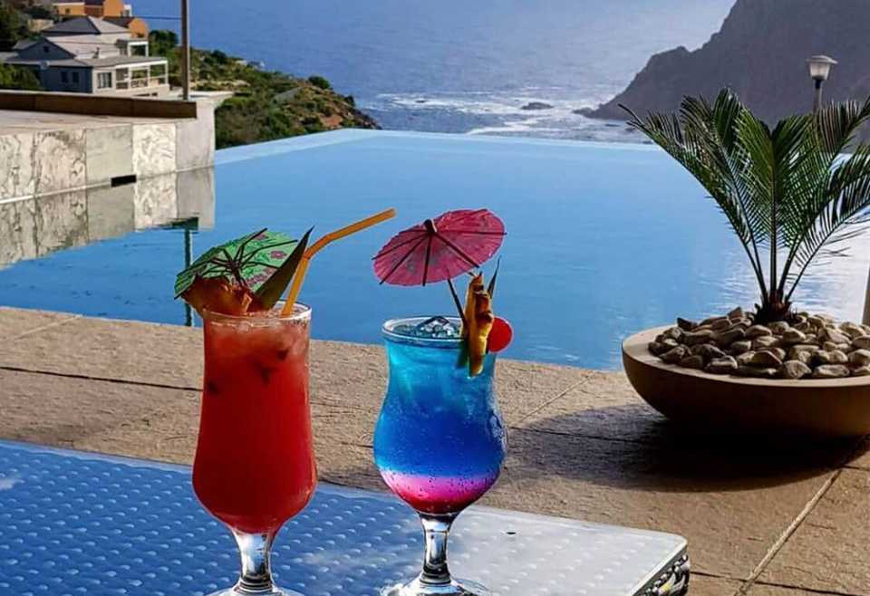 Two colorful cocktails on a table overlooking an infinity pool and ocean.