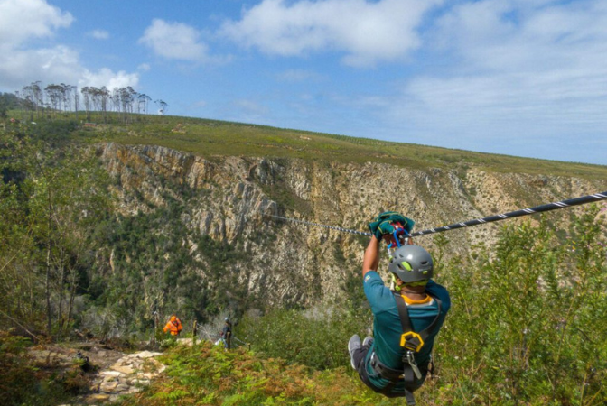 Person ziplining across a canyon on a bright, sunny day.