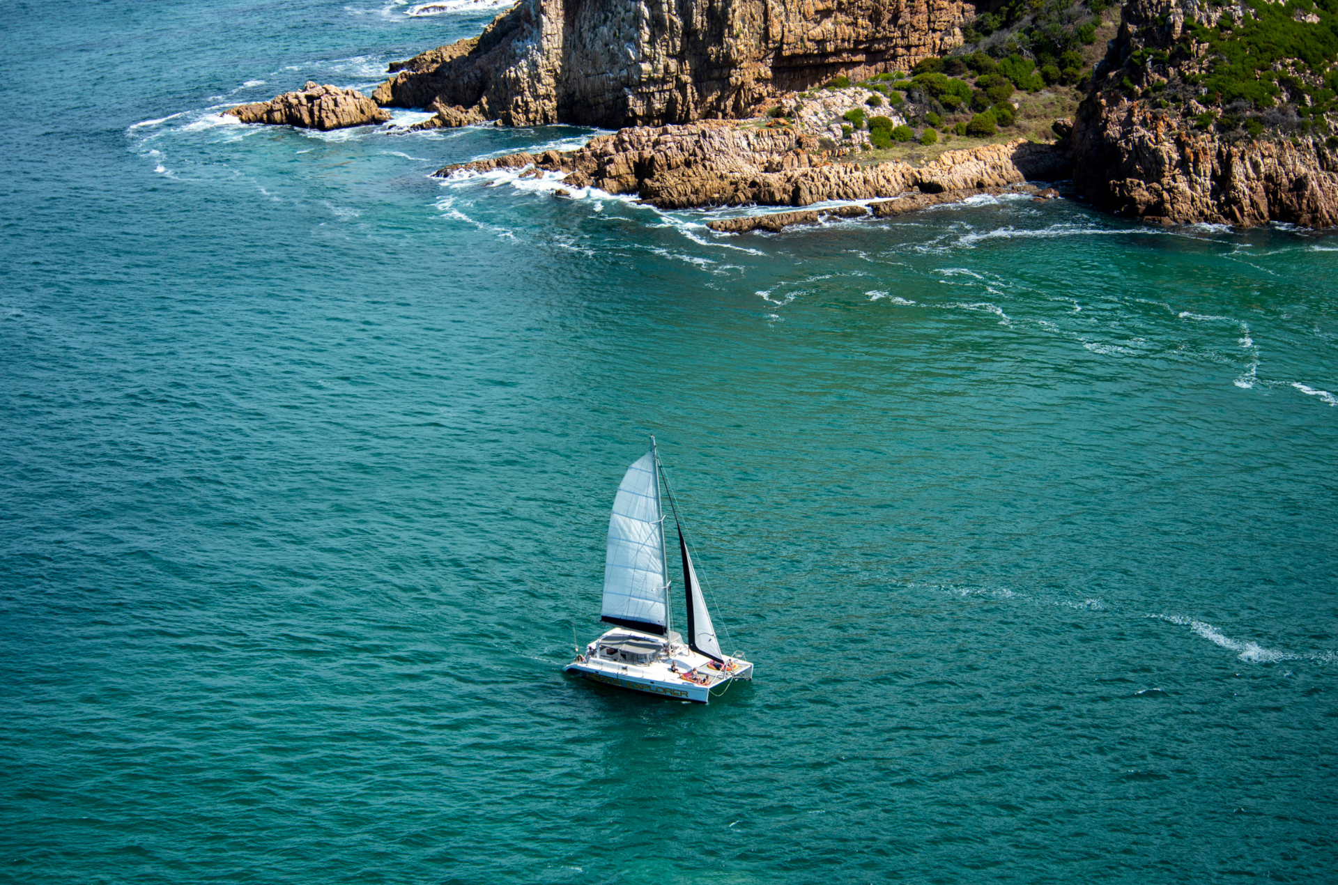 Sailboat on teal water near rocky, brown cliffs.