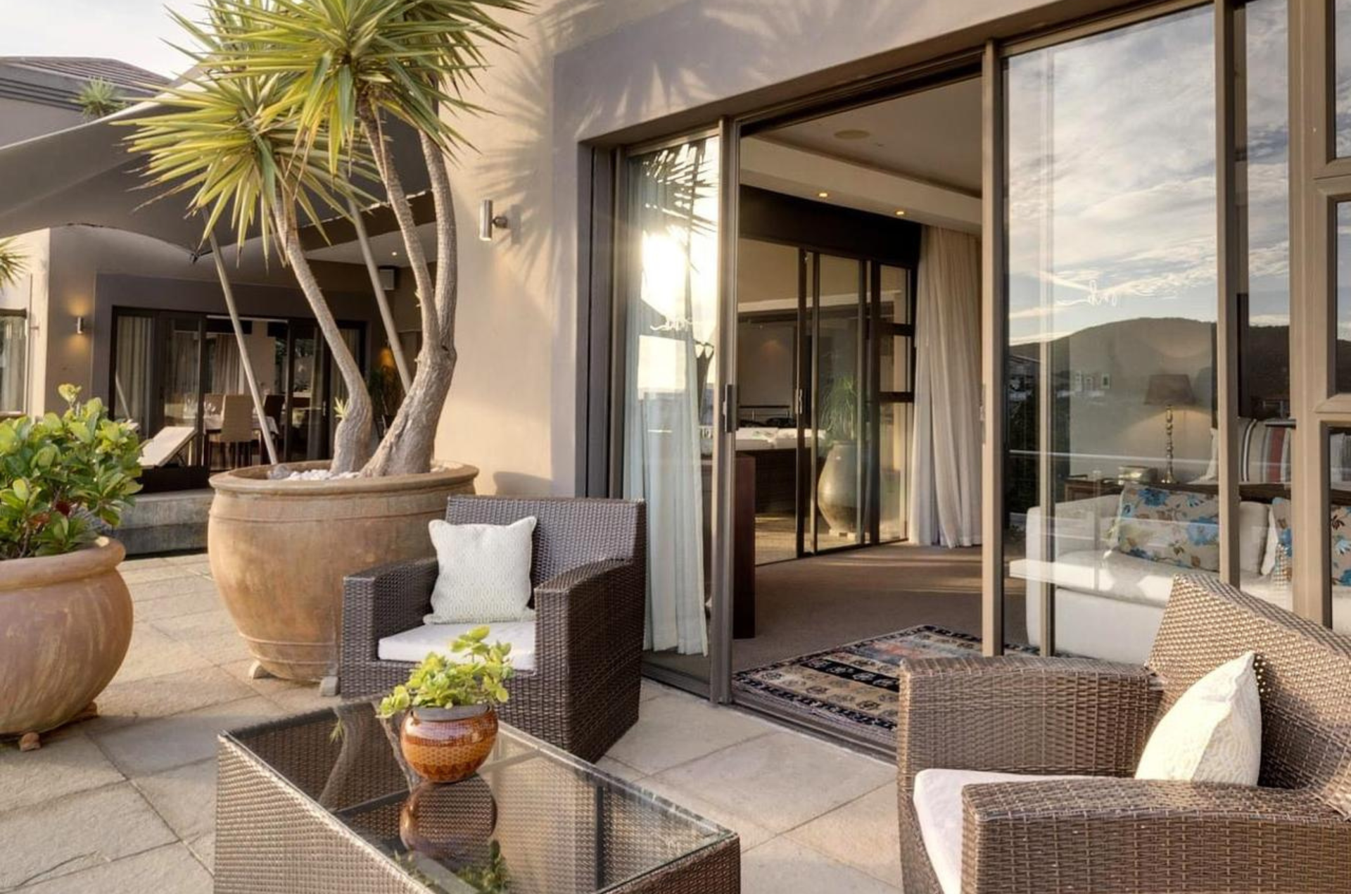 Patio with wicker furniture, potted plants, and open sliding glass doors leading to interior.