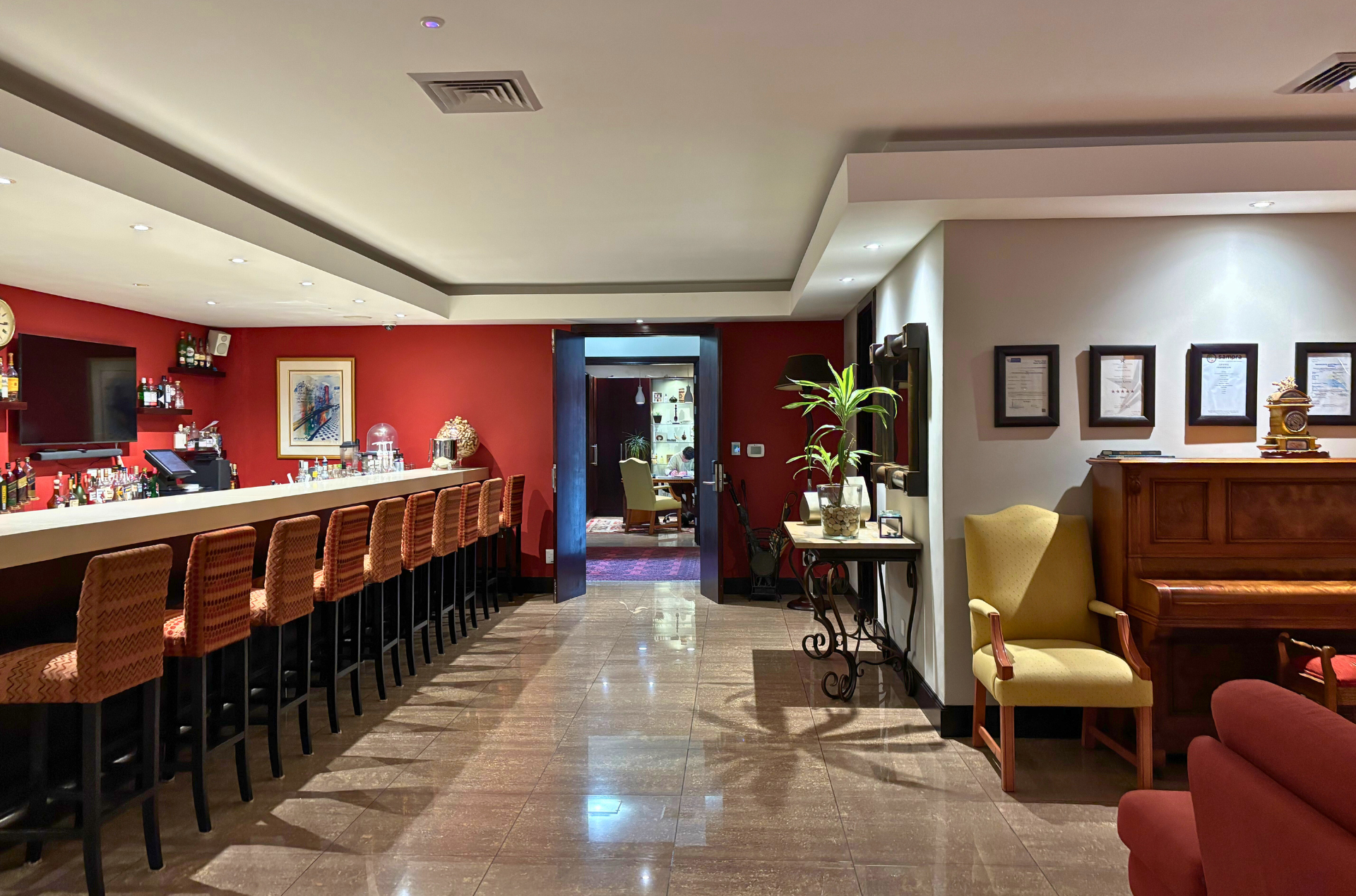 Interior of a bar with red walls, a long counter with barstools, and a piano.
