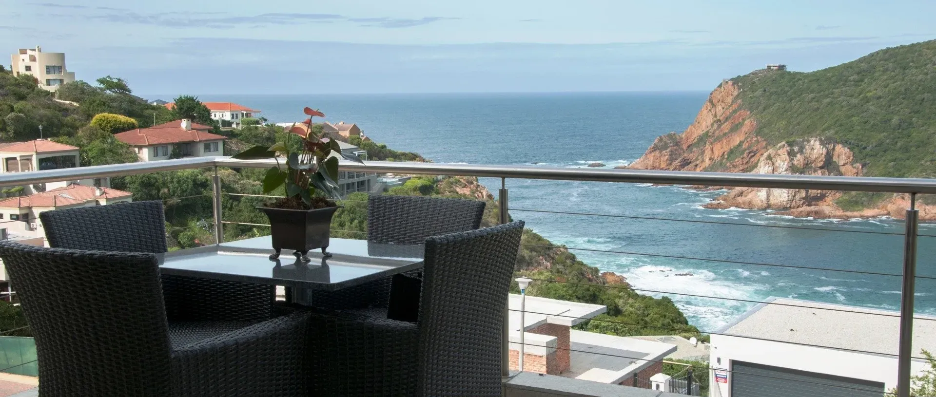 A balcony with a table and chairs overlooking the ocean and hills.