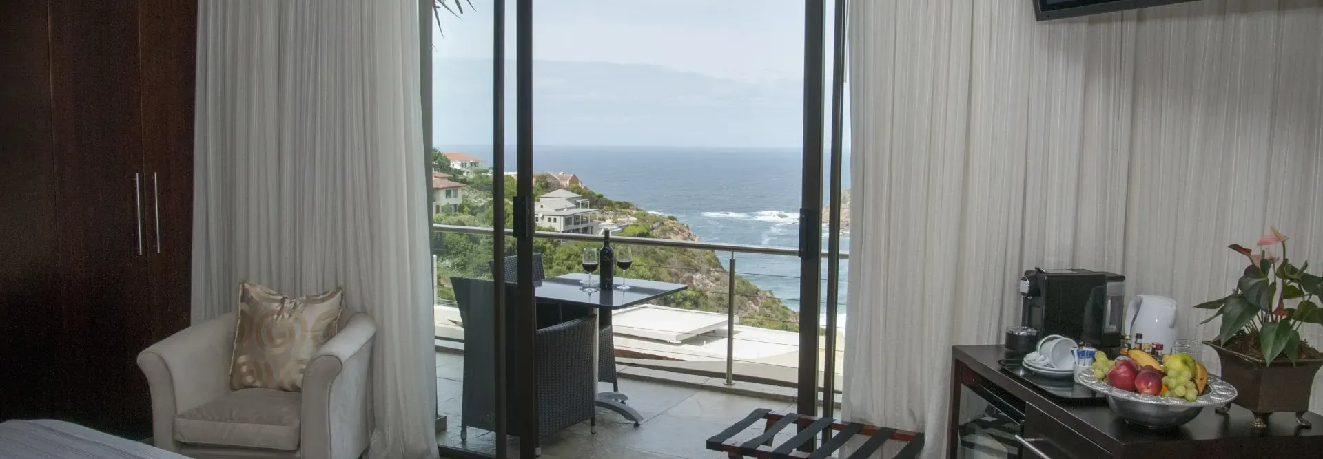 A hotel room overlooking the ocean. Includes a balcony, chair, table, and large sliding doors.