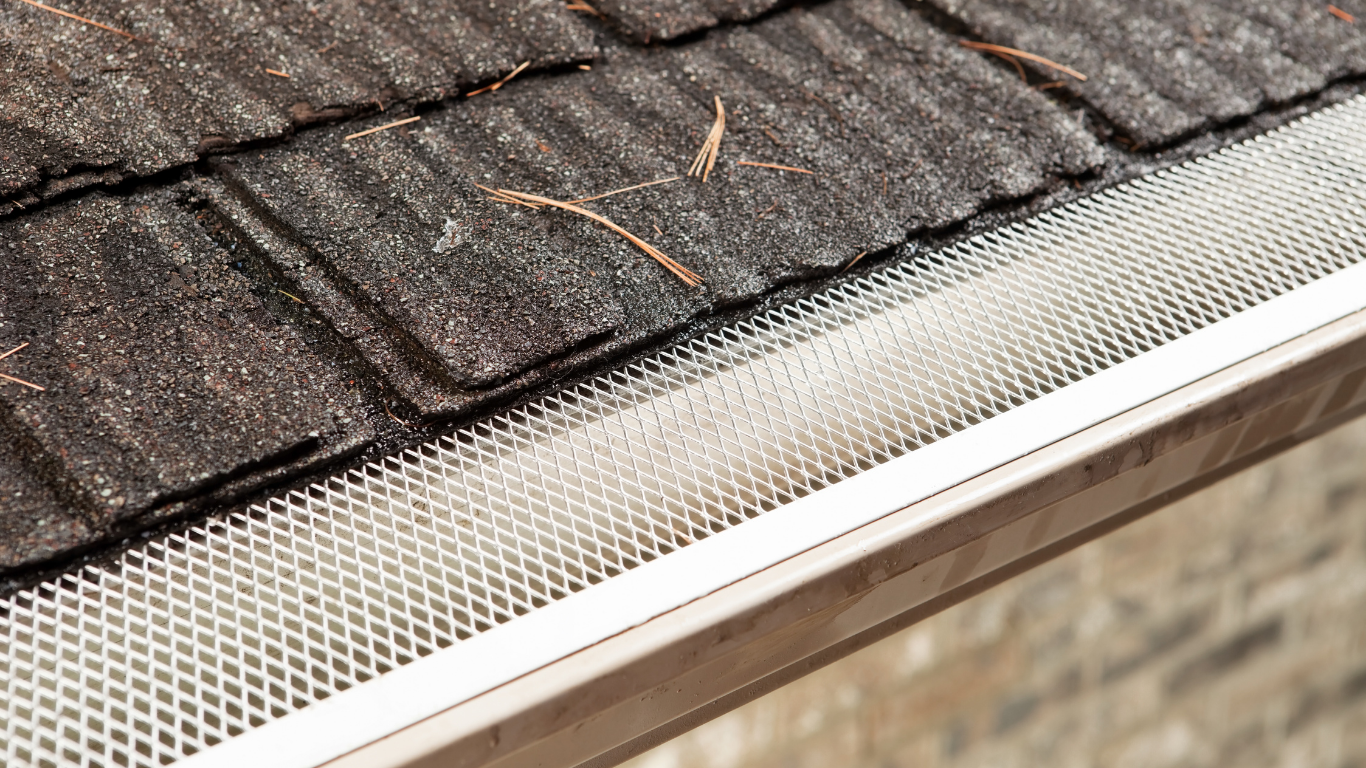 A close up of a gutter on a roof with shingles.