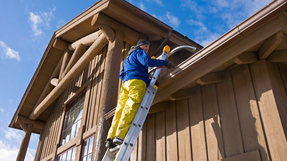 A man is standing on a ladder on the side of a wooden building.
