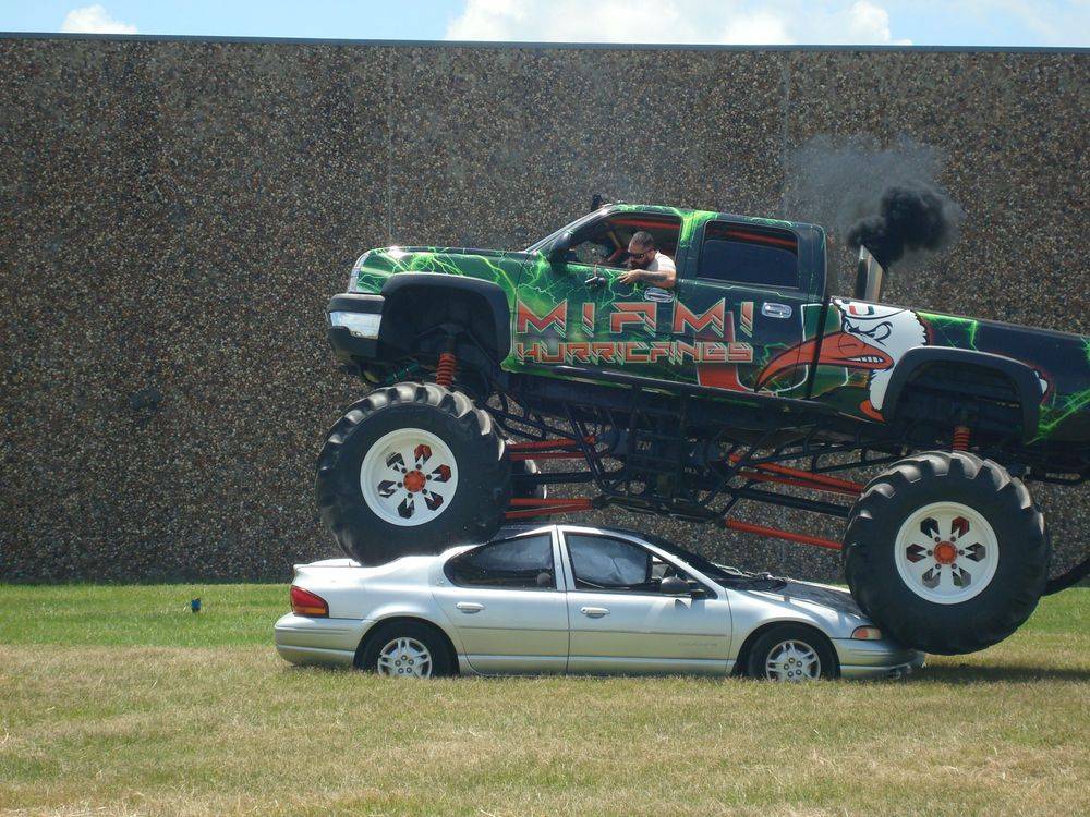 A monster truck is sitting on top of a silver car