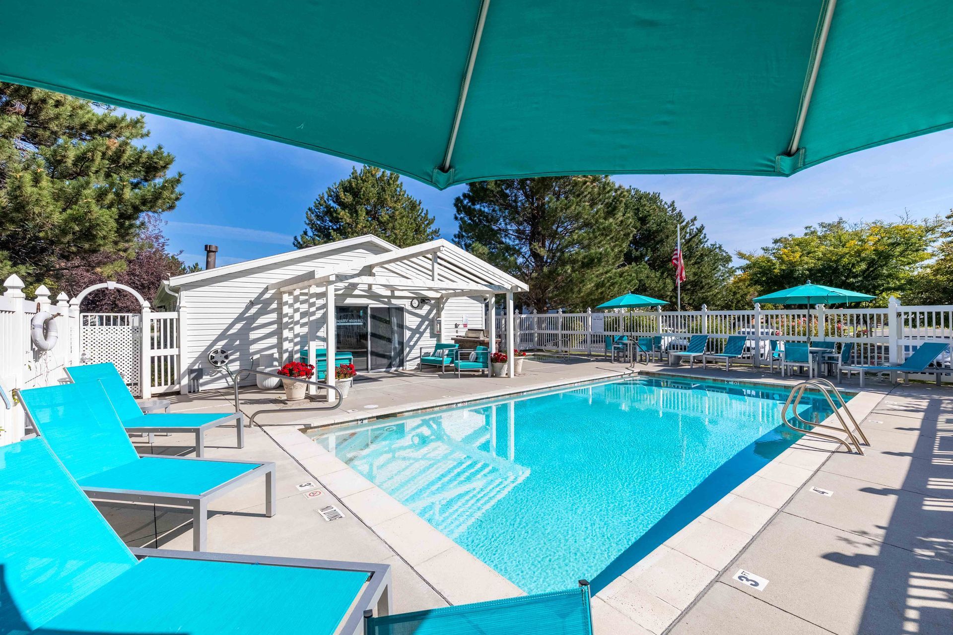 Pool with turquoise lounge chairs, umbrellas, and white gazebo on a sunny day.