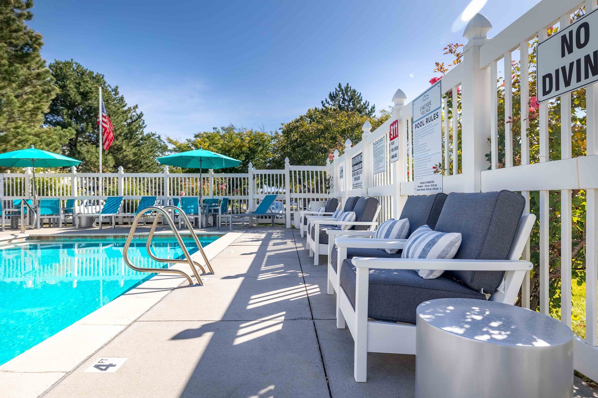 Poolside seating area with lounge chairs, umbrella-shaded tables, and a pool on a sunny day.