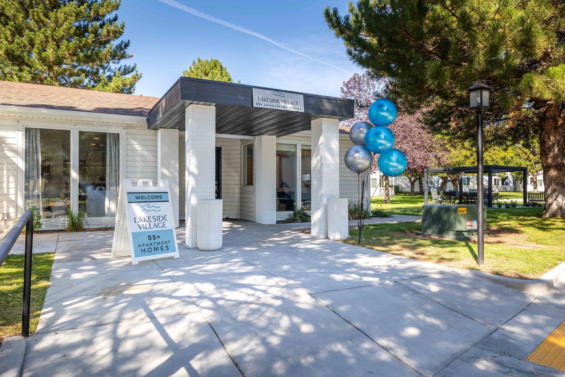 Entrance to a white building with an overhang. Balloons and a sign are in front.