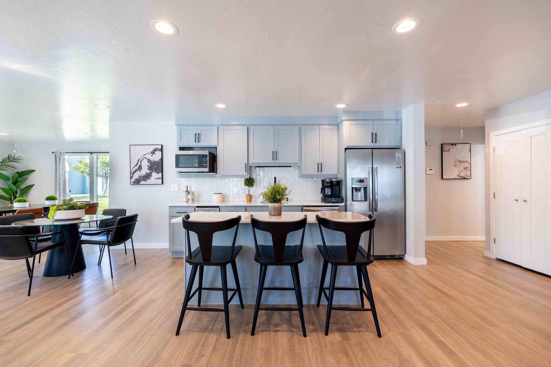 Kitchen with light blue cabinets, stainless steel appliances, and a breakfast bar with three black chairs.