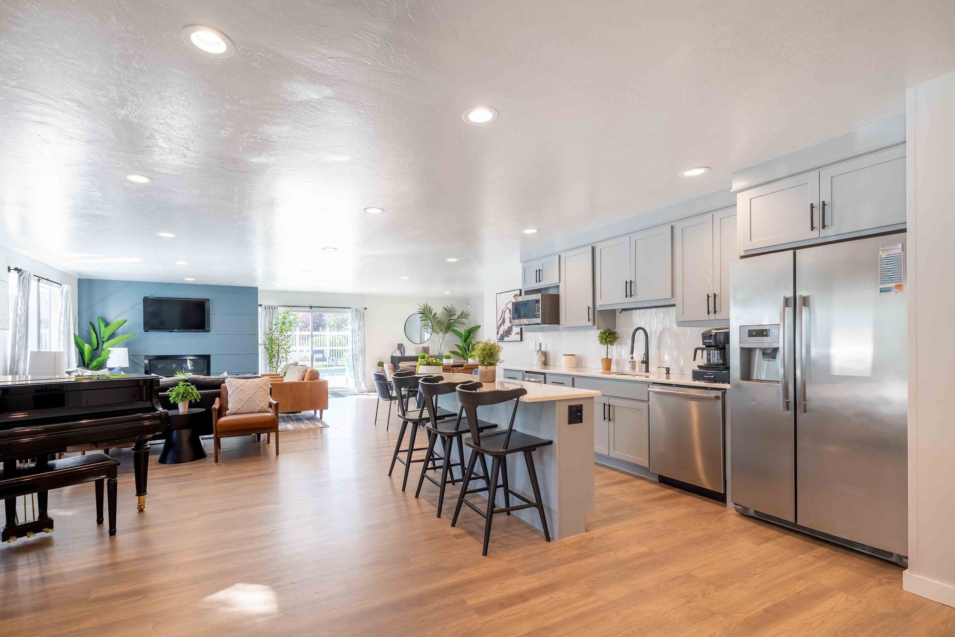Open-concept kitchen and living area with hardwood floors, stainless steel appliances, and a piano.