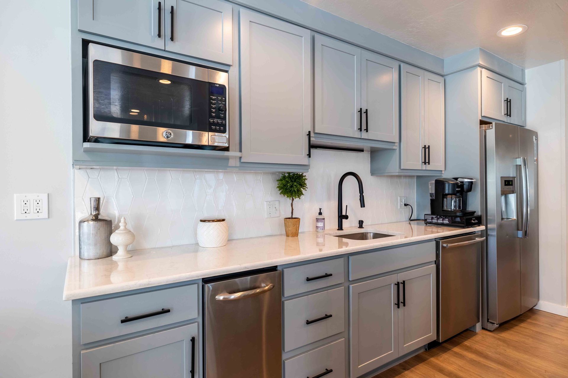 Modern kitchen with light blue cabinets, stainless steel appliances, and white countertops.