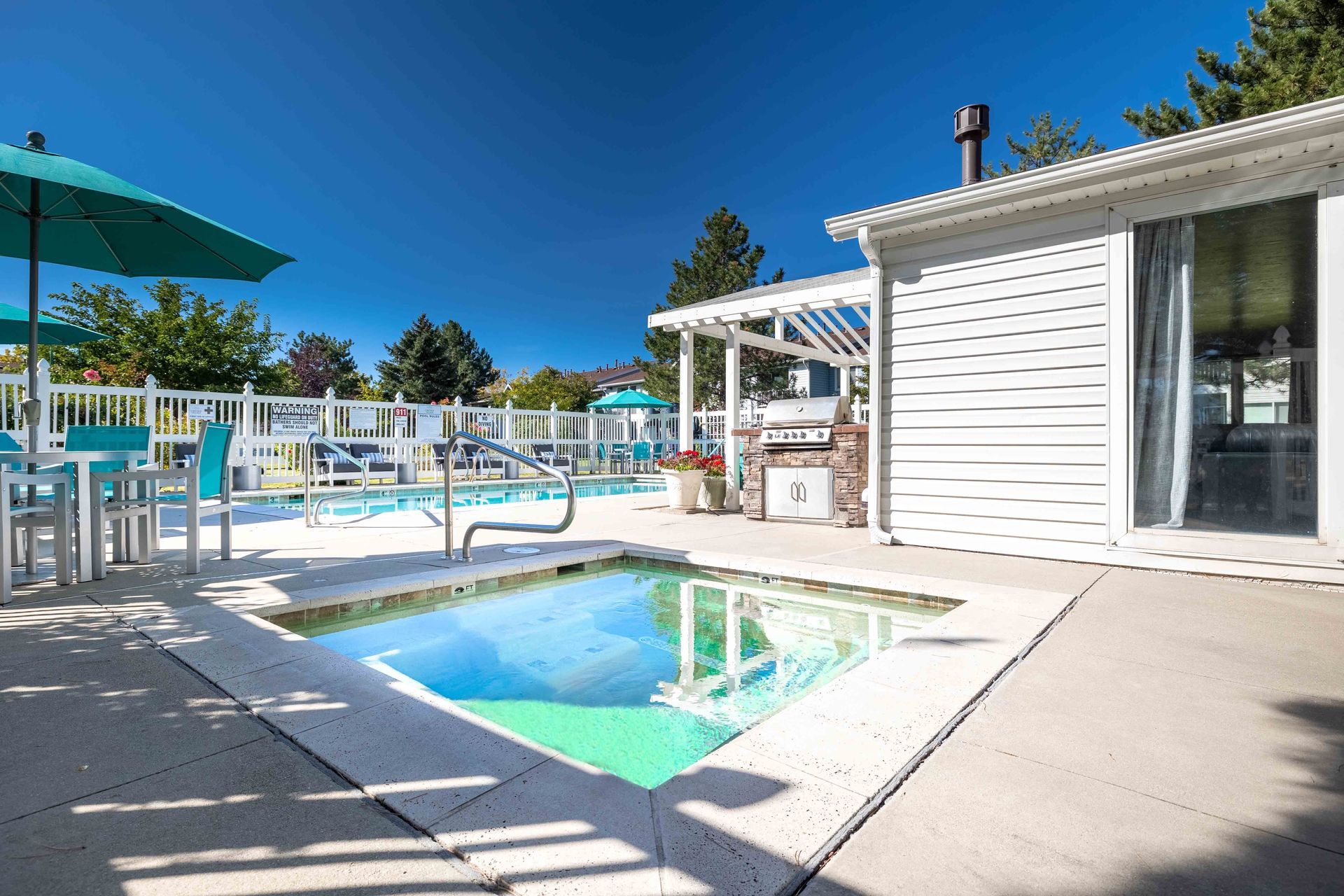 Outdoor pool area with small pool, patio furniture, grill, and bright blue umbrellas.