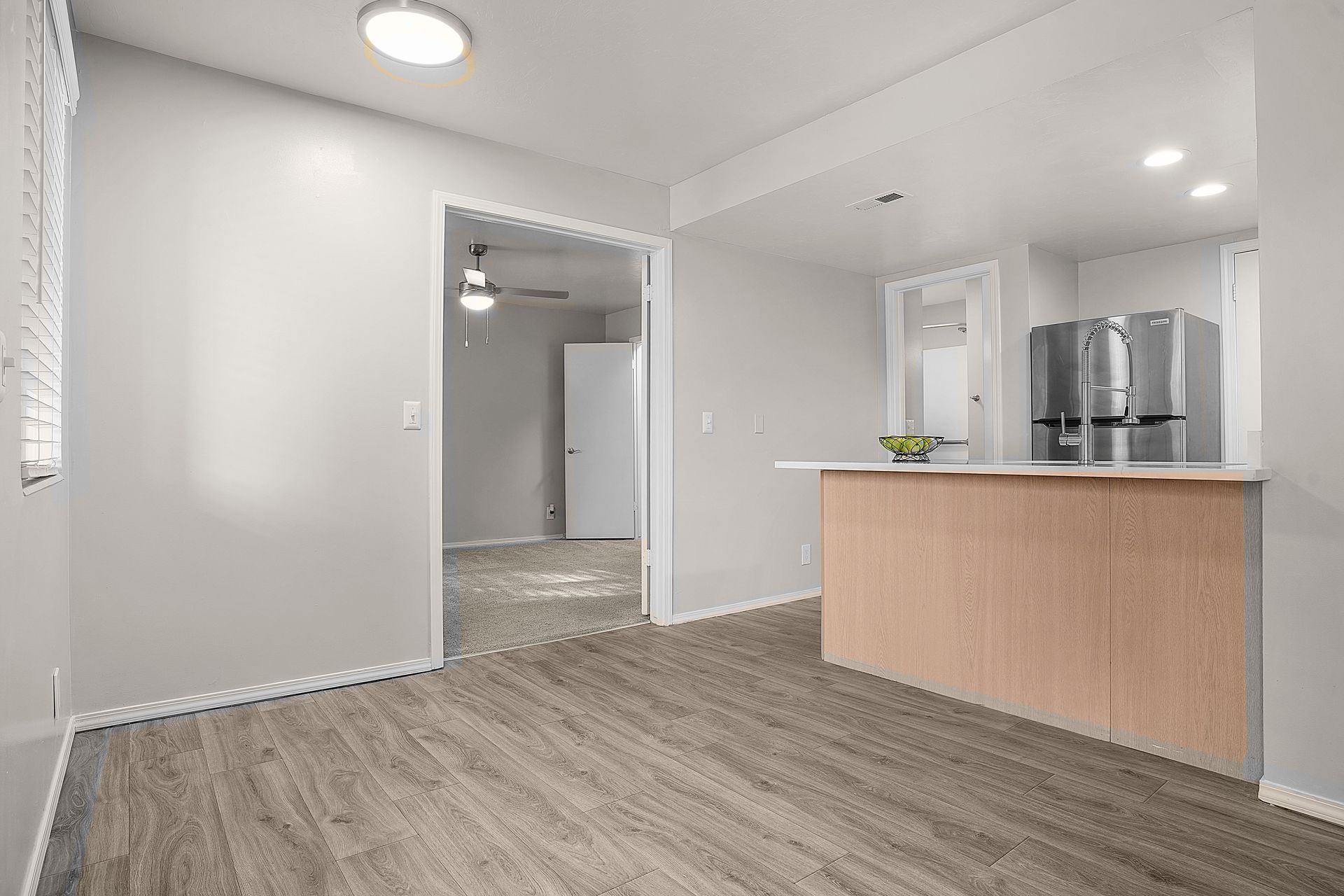 Interior of an apartment with light wood flooring, kitchen island, and doorway leading to another room.