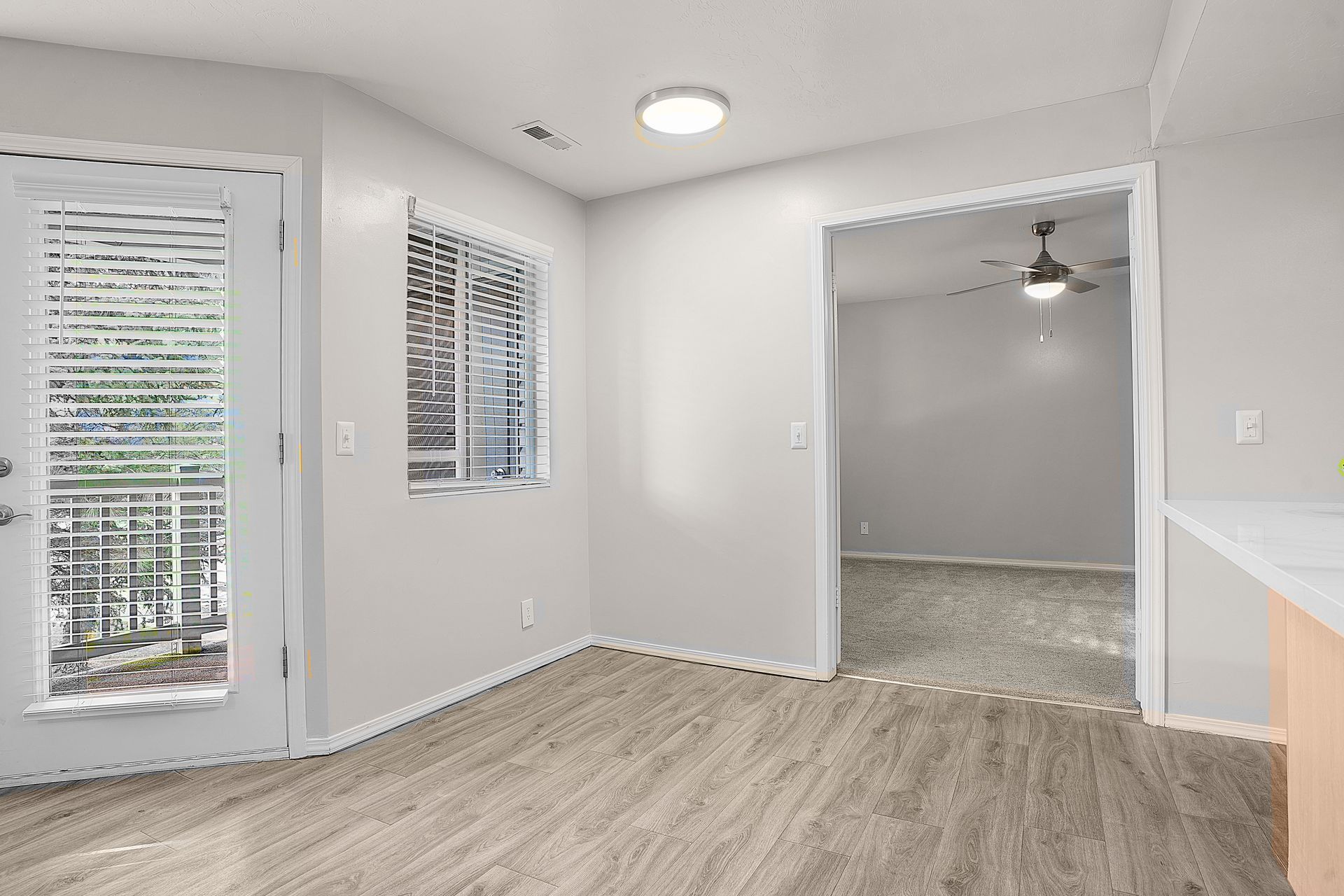 Interior room with door to balcony, window, opening to another room. Light wood floors, white walls.