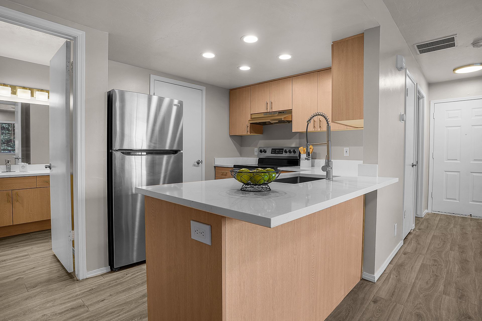 Kitchen with stainless steel refrigerator, light wood cabinets, white countertops, and island.
