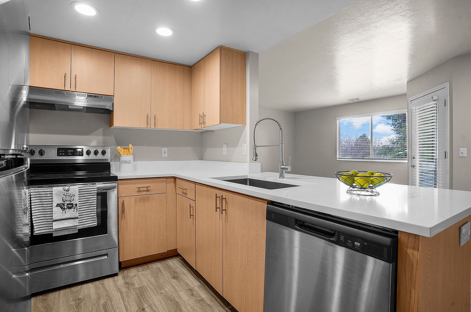 Modern kitchen with light wood cabinets, stainless steel appliances, and white countertops.