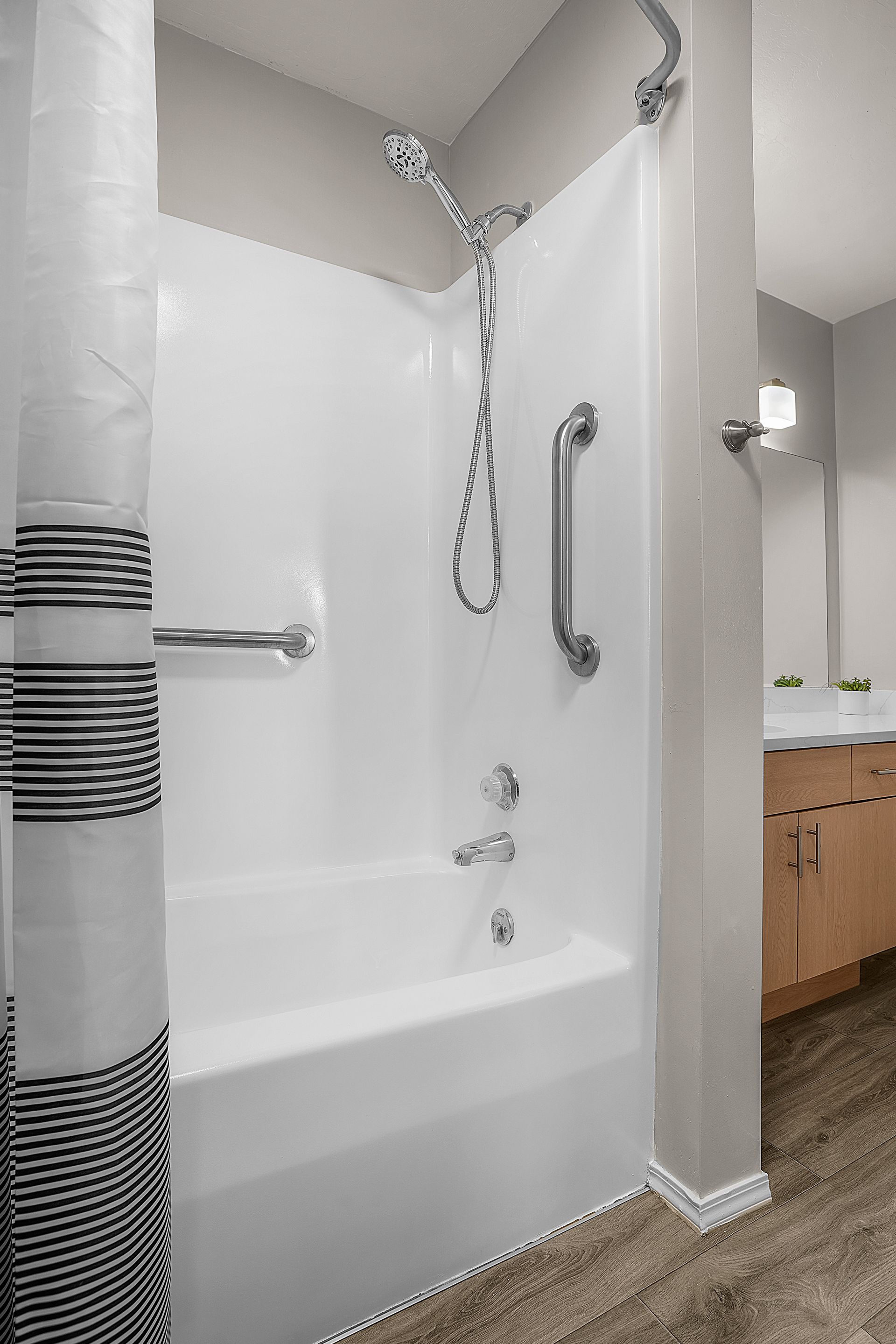 White shower with grab bars; shower curtain left, vanity right.